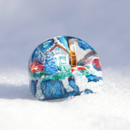 Colorful winter scene inside glass paperweight on snow.