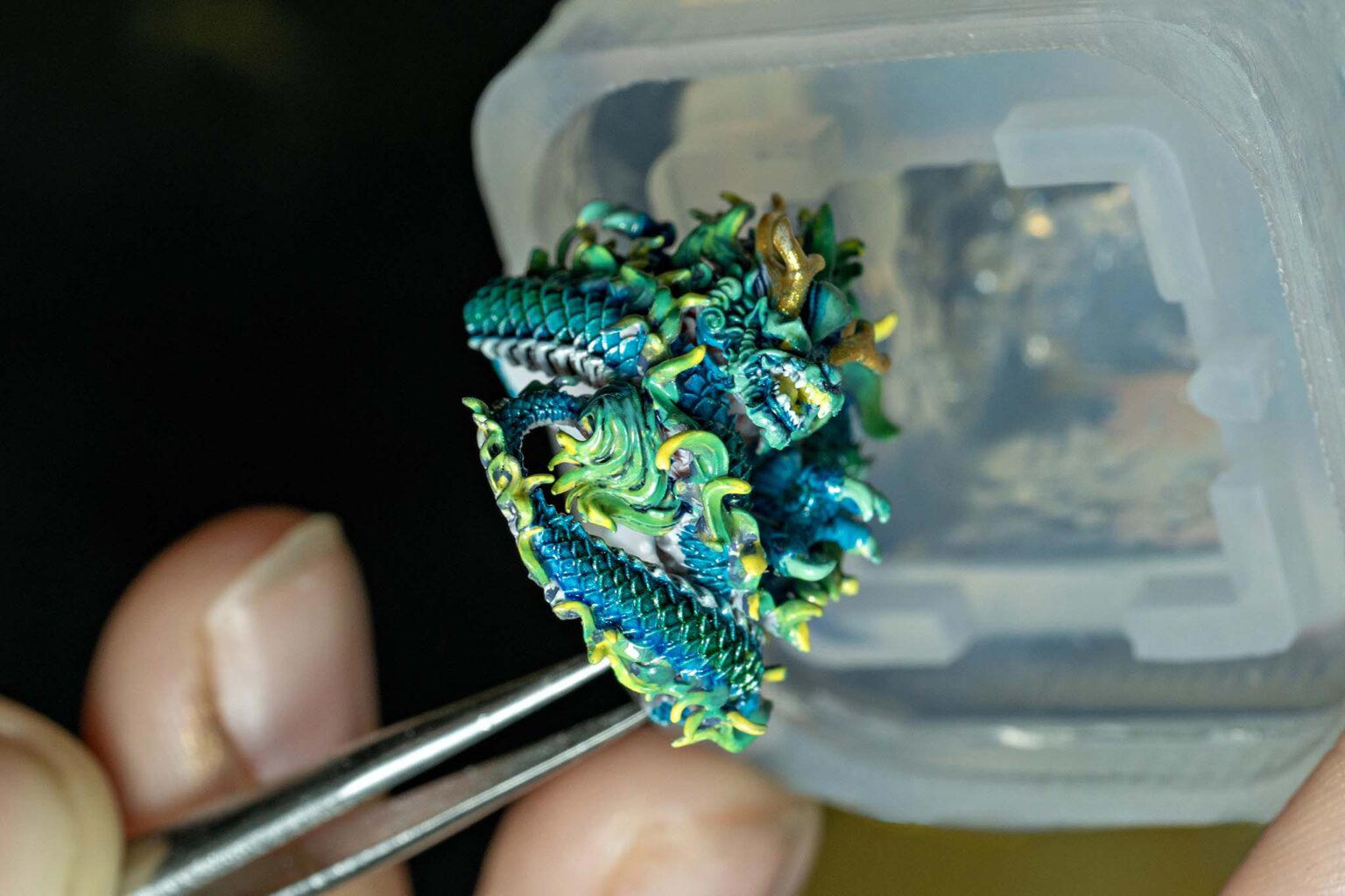 Detailed miniature dragon figurine held by tweezers.