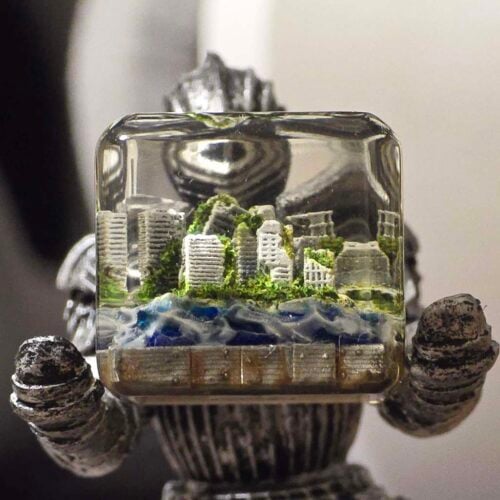 Miniature cityscape in a glass cube held by robot hands.